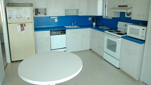 A kitchen with white cabinets, a blue countertop, a white table, and a refrigerator.