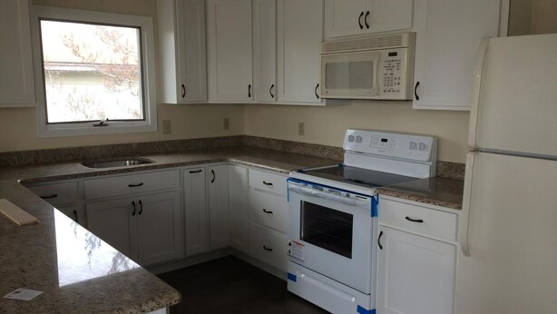 A kitchen with white cabinets, a built-in microwave, a stove, and a refrigerator.
