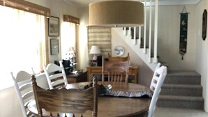 Zona pranzo con tavolo e sedie in legno, una lampada a sospensione e una scala che conduce a un piano superiore.