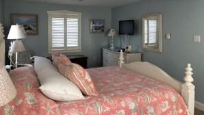 Una camera da letto con un letto, una cassettiera, una televisione e due finestre.