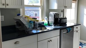 Cucina con mobili bianchi, piano di lavoro nero e finestra con persiane.