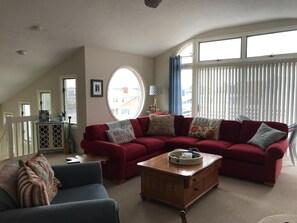 A living room with a red sectional sofa, a blue armchair, a wooden coffee table, and a large window with blinds. - 4 bedroom accommodation in Harvey Cedars (Harvey Cedars)