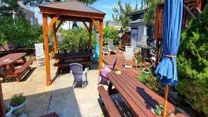 Eine Holzterrasse mit Picknicktischen und -stühlen, einer Holzpergola und einem blauen Sonnenschirm.