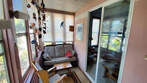 Ein gemütliches Zimmer mit einer Couch, Holzstühlen, einem Tisch und einem großen Fenster mit Jalousien.