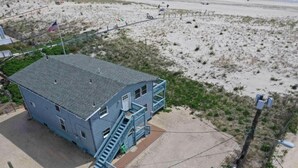 A two-story building with a blue exterior, a front staircase, and a flagpole with an American flag. - Ocean front Duplex Brant Beach 1st Floor (Brant Beach)