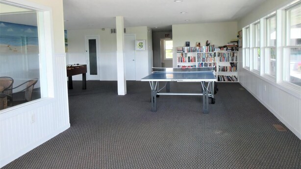 A room with a ping pong table, a bookshelf, and a view through a window.