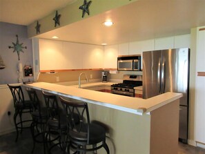 A modern kitchen with a central island, stainless steel appliances, and bar stools.