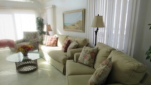 Ein Wohnzimmer mit einem beigefarbenen Sofa, einem Glastisch und einer Lampe.