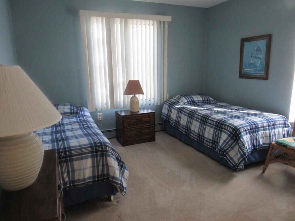 Une chambre avec deux lits, une table de chevet avec une lampe, une chaise et une fenêtre avec des stores.