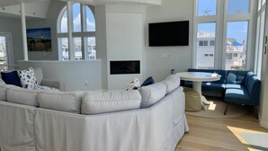 A modern living room with a sectional sofa, a flat-screen TV, and large windows with starfish decorations. - Surf City Oceanfront With Panoramic Views (Surf City)