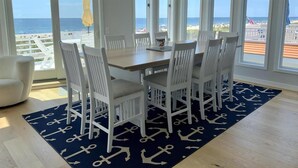 A dining area with a table and chairs, large windows, and a view of the beach. - Surf City Oceanfront With Panoramic Views (Surf City)