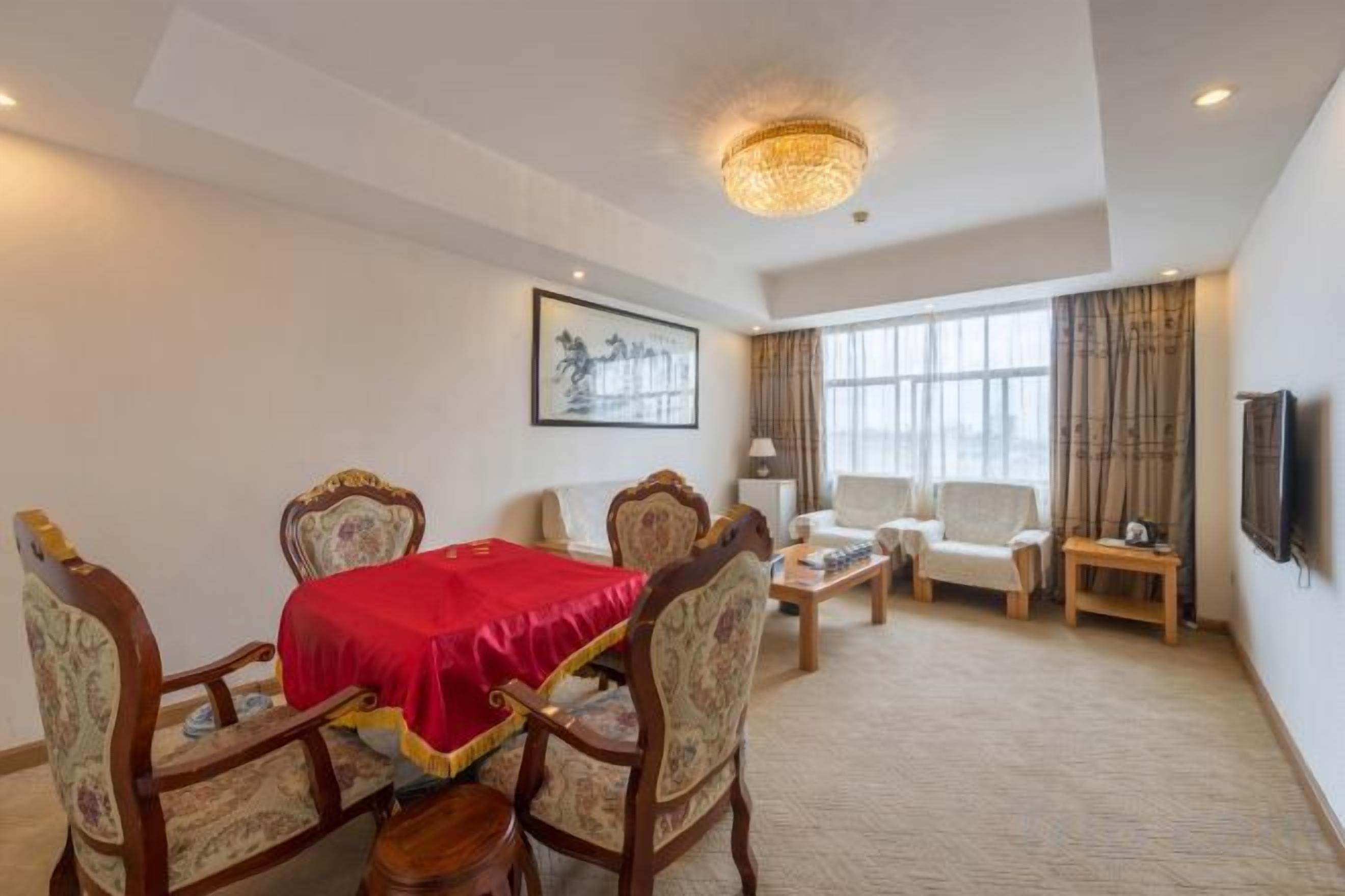 A hotel room with a dining table, chairs, a sofa, a TV, and a large window.