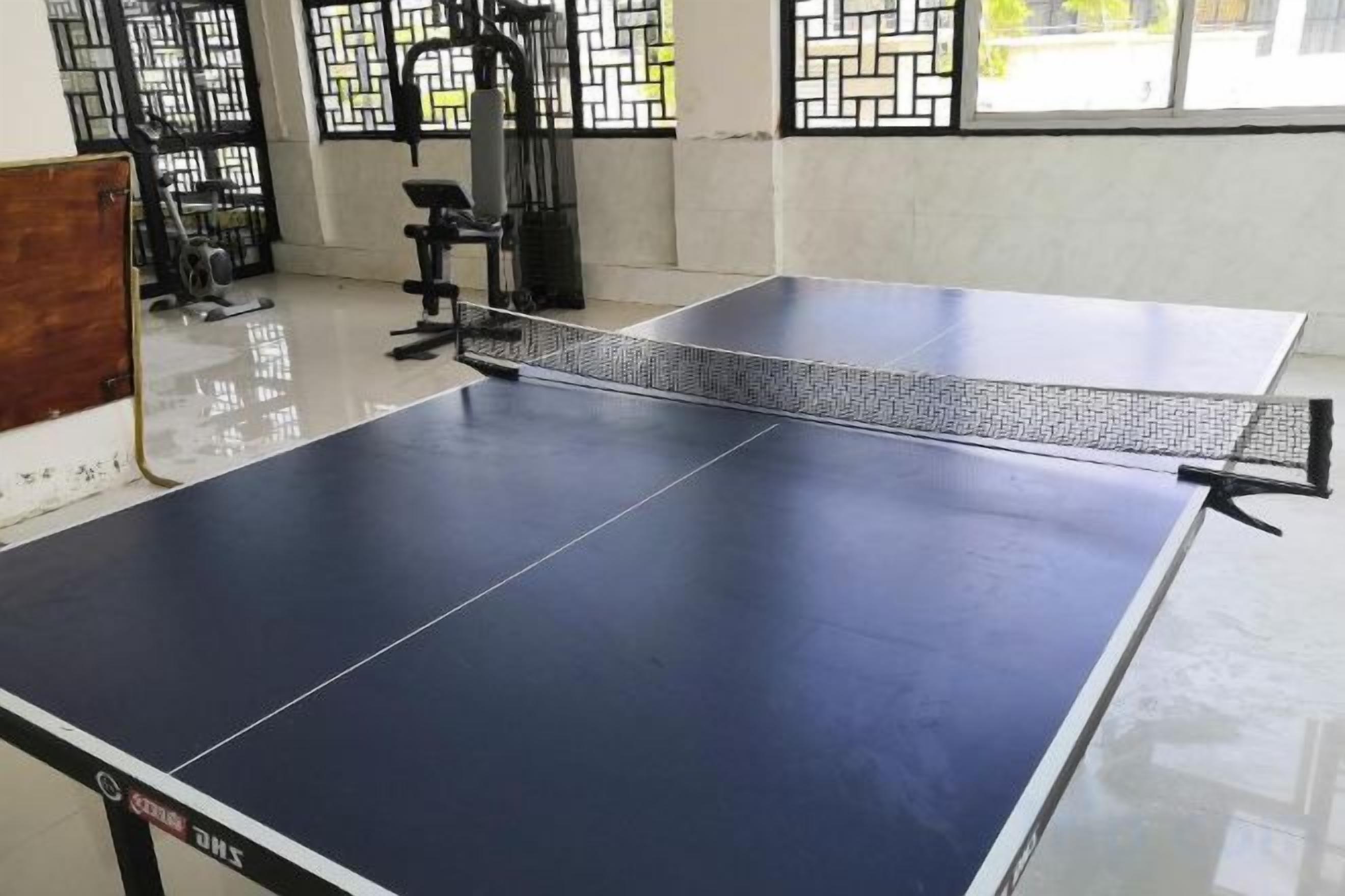 Una mesa de ping pong en una habitación con equipo de ejercicio y un ventanal con vistas.