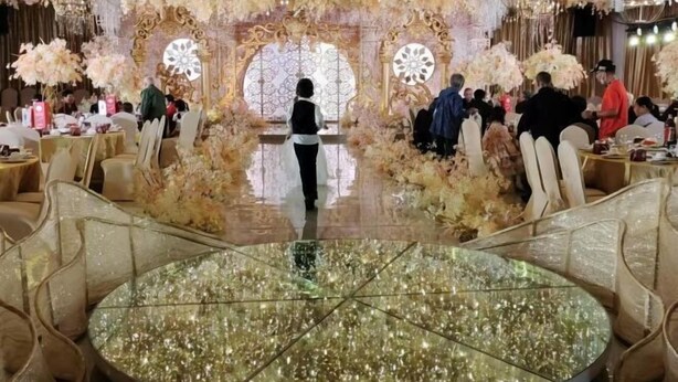 Un espace événementiel élégant, agrémenté de décorations raffinées, avec une table centrale aux reflets chatoyants et des invités placés à des tables rondes.