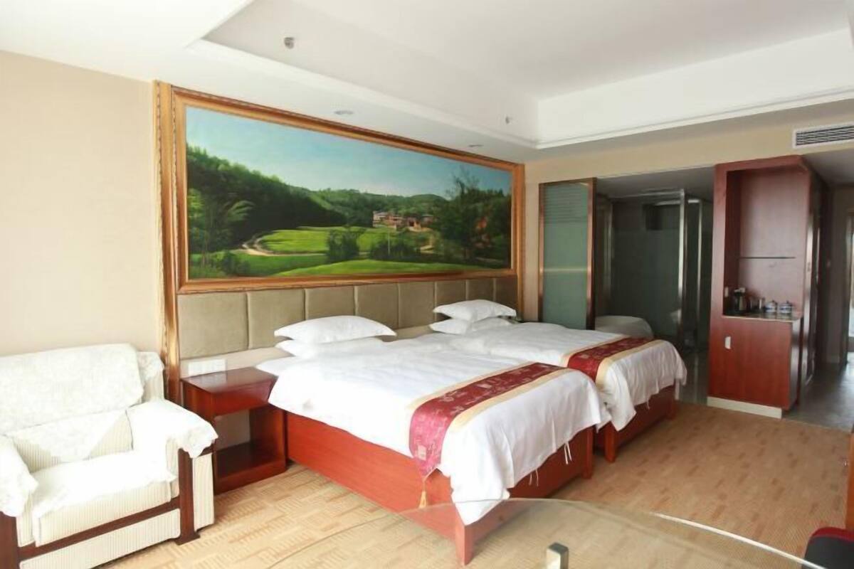A hotel room with two beds, a painting of a landscape, a wooden wardrobe, and a chair.