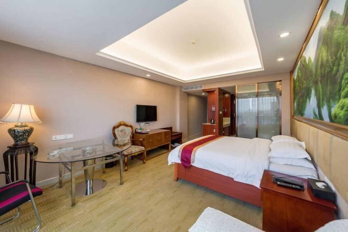 Une chambre d’hôtel avec un lit, un bureau, une chaise, une télévision et un tableau au mur.
