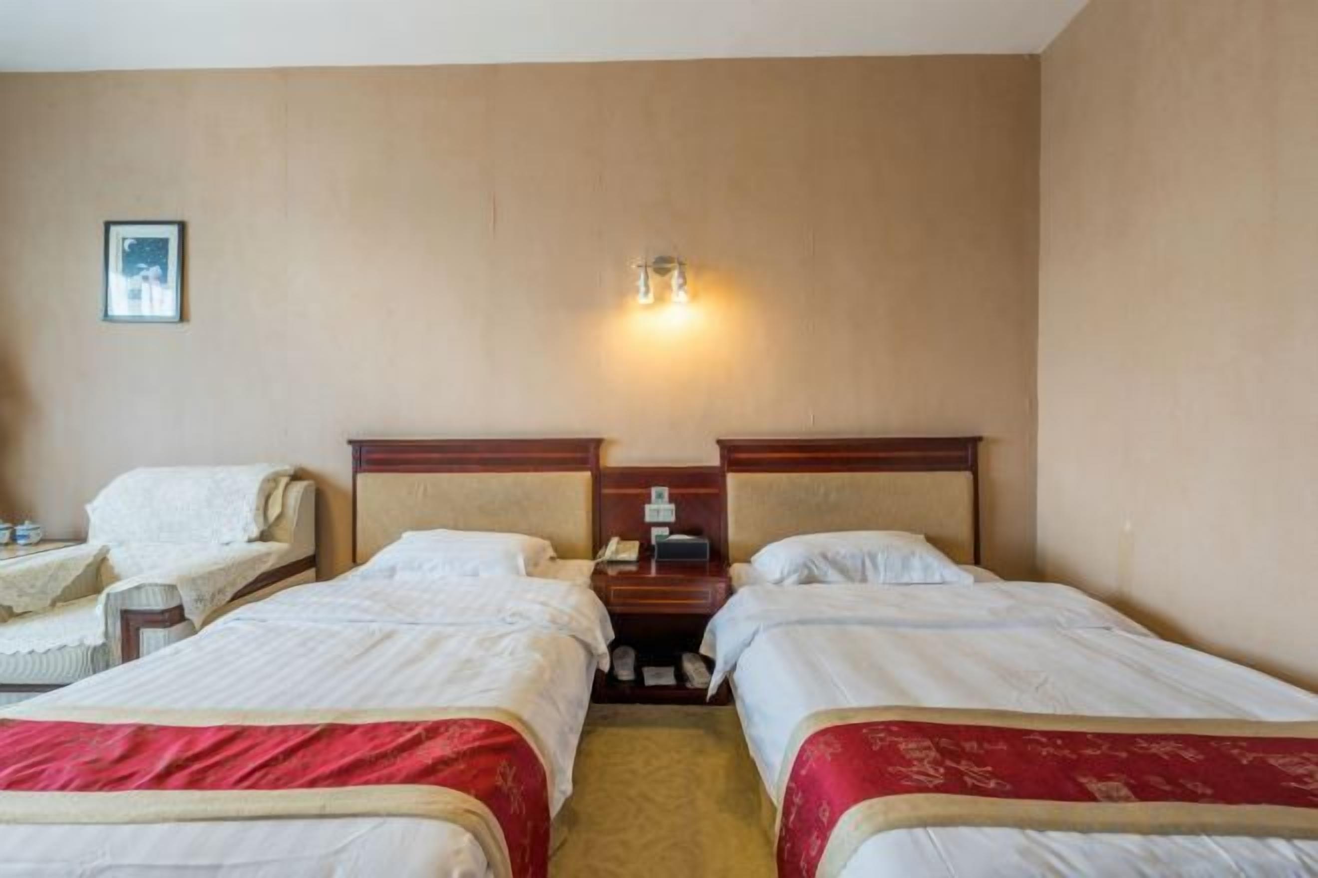 A hotel room with two beds, a nightstand, a lamp, and a chair.