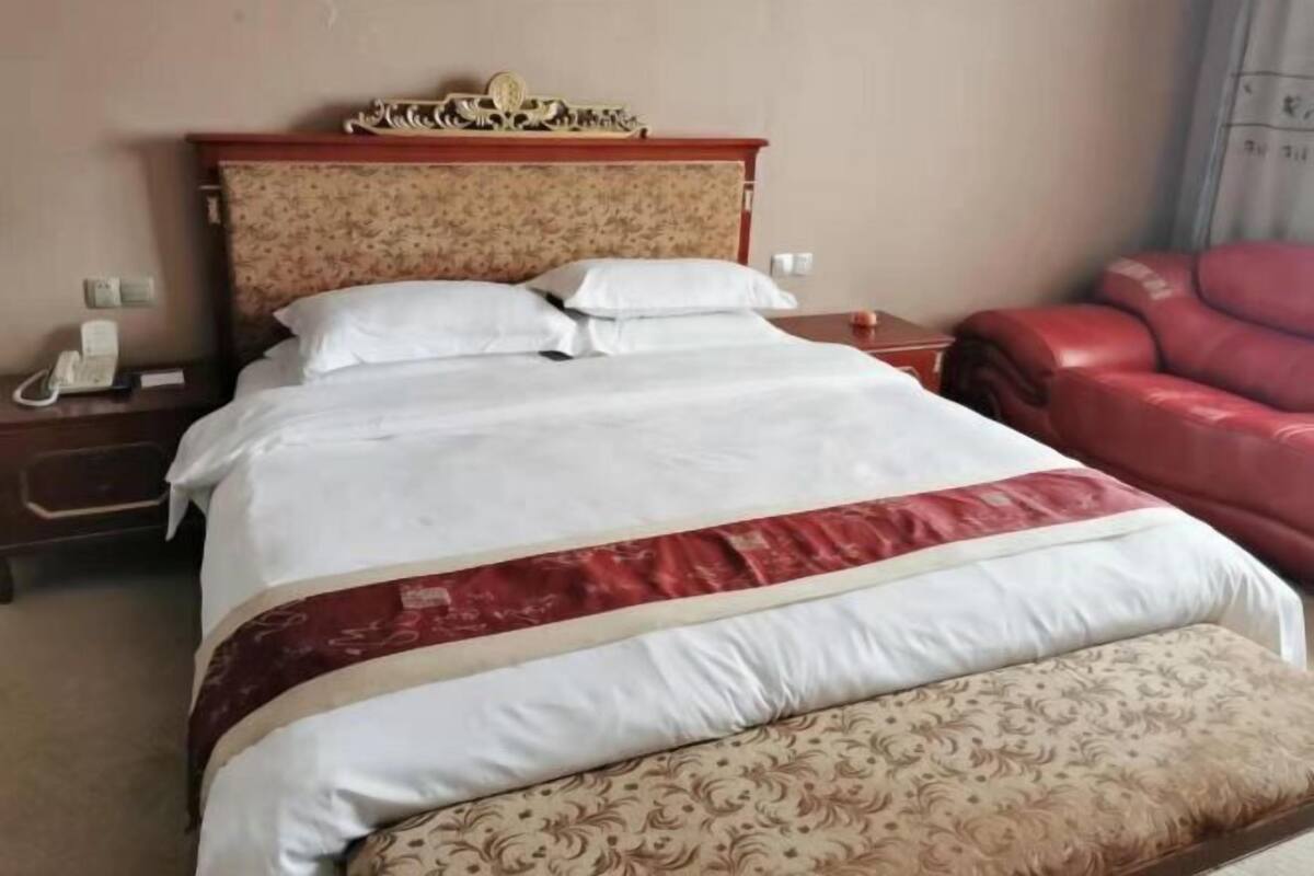 A hotel room with a bed, a bedside table with a phone, a red leather chair, and a patterned headboard.