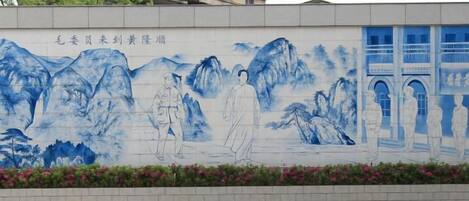 A mural with figures and mountains, a building with a sign, and a paved area with yellow lines.