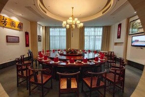 Une salle de conférence avec une table ronde, des chaises, un lustre et un téléviseur fixé au mur.