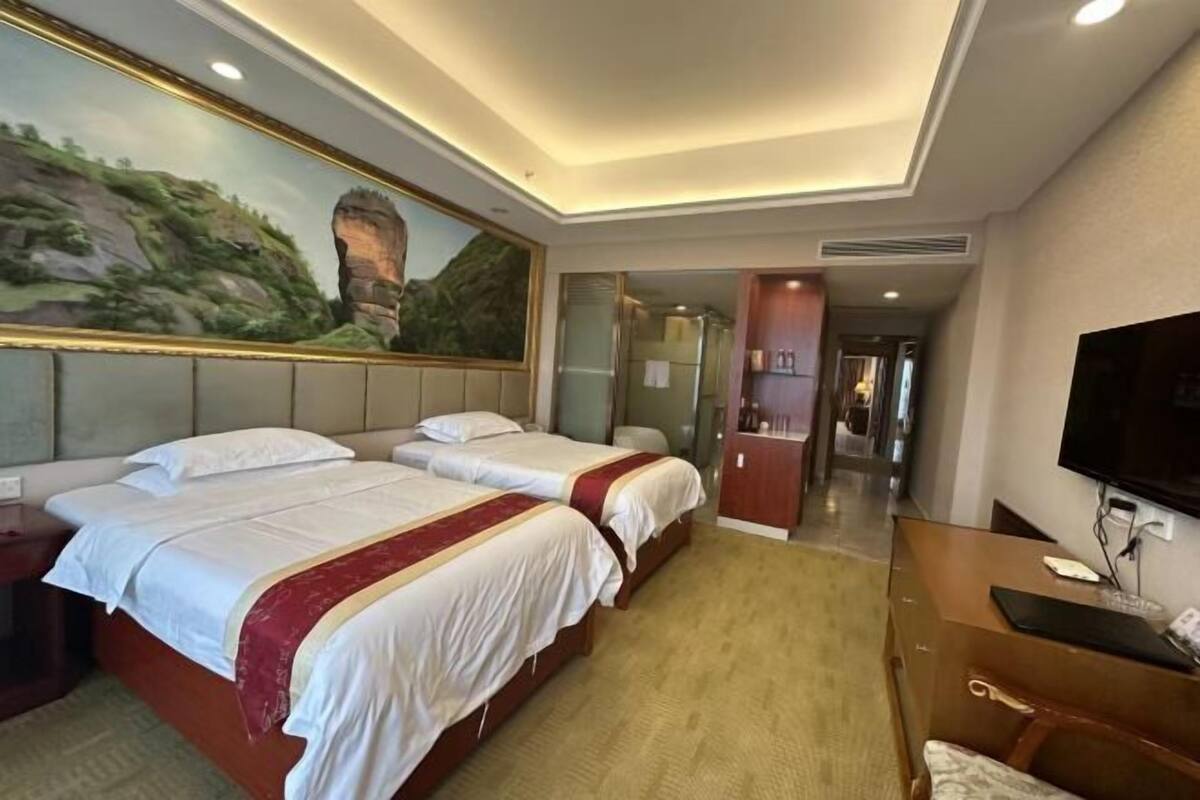 A hotel room with two beds, a television, a desk, and a mirror.