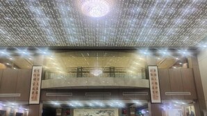 Un hall d’hôtel avec un plafond haut, un grand comptoir d’accueil et un lustre.