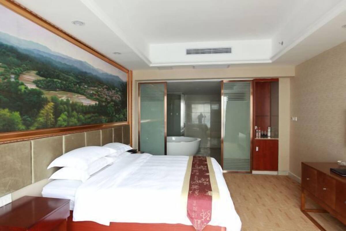 A hotel room with a bed, a painting, a bathroom, and a wardrobe.