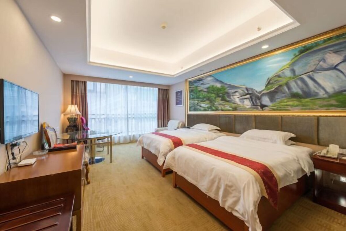 Une chambre d’hôtel avec deux lits, un bureau, une télévision et un tableau au mur.