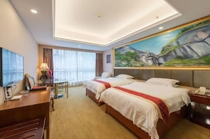 Habitación de hotel con dos camas, un escritorio, un televisor y un cuadro en la pared.