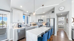 A modern kitchen with white cabinets, stainless steel appliances, a marble island, and blue bar stools.