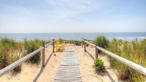 A wooden boardwalk leading to a beach with a wooden fence and a yellow bench.