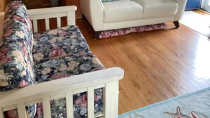 Ein Zimmer mit einem weißen Sofa, einer gepolsterten Bank mit Blumenmuster, Holzvertäfelung, einer blauen Tür und einem Bild an der Wand.