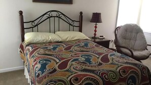 A bed with a patterned bedspread, a chair, a nightstand with a lamp, and a framed picture on the wall. - 4 bedroom accommodation in Barnegat Light (Barnegat Light)