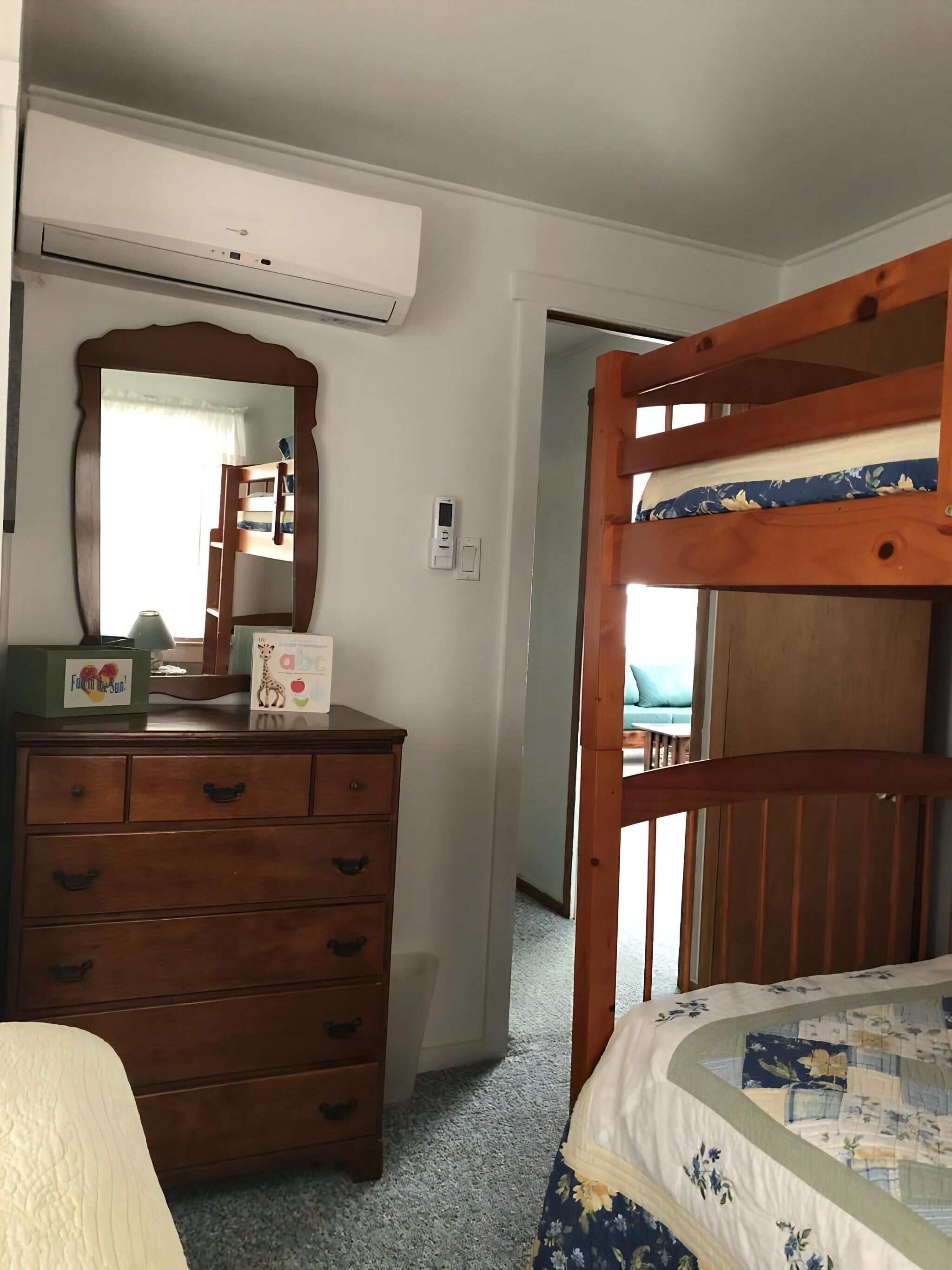 A bedroom with a bunk bed, a dresser with drawers, a mirror, and a thermostat.