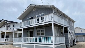 A two-story house with a balcony, a front porch, and a visible staircase leading to the upper floor. - Ocean block duplex located in the heart of Surf City. (Surf City)