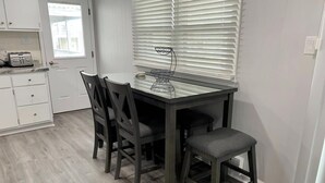 A kitchen with a dining table, chairs, a toaster, and a window with blinds. - Ocean block duplex located in the heart of Surf City. (Surf City)