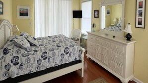 Een slaapkamer met een bed, een dressoir, een spiegel en een plafondventilator.