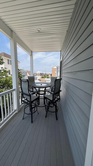A covered outdoor seating area with a table and chairs, a railing, and a view of neighboring houses.