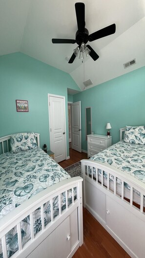 Une chambre avec deux lits, un ventilateur de plafond, une porte et un miroir fixé au mur.
