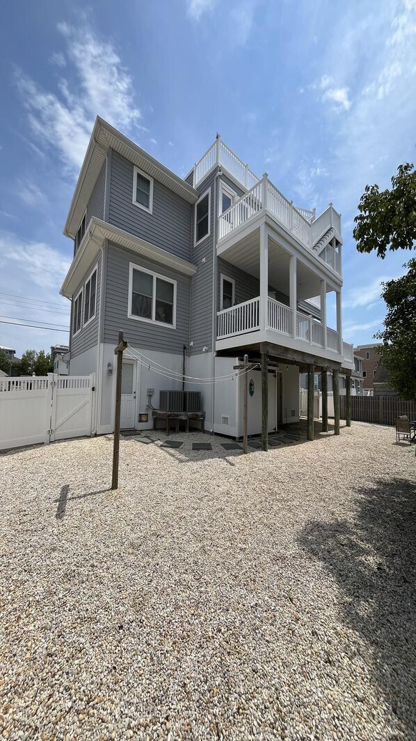 A two-story house with a balcony, a gravel driveway, and a white fence.