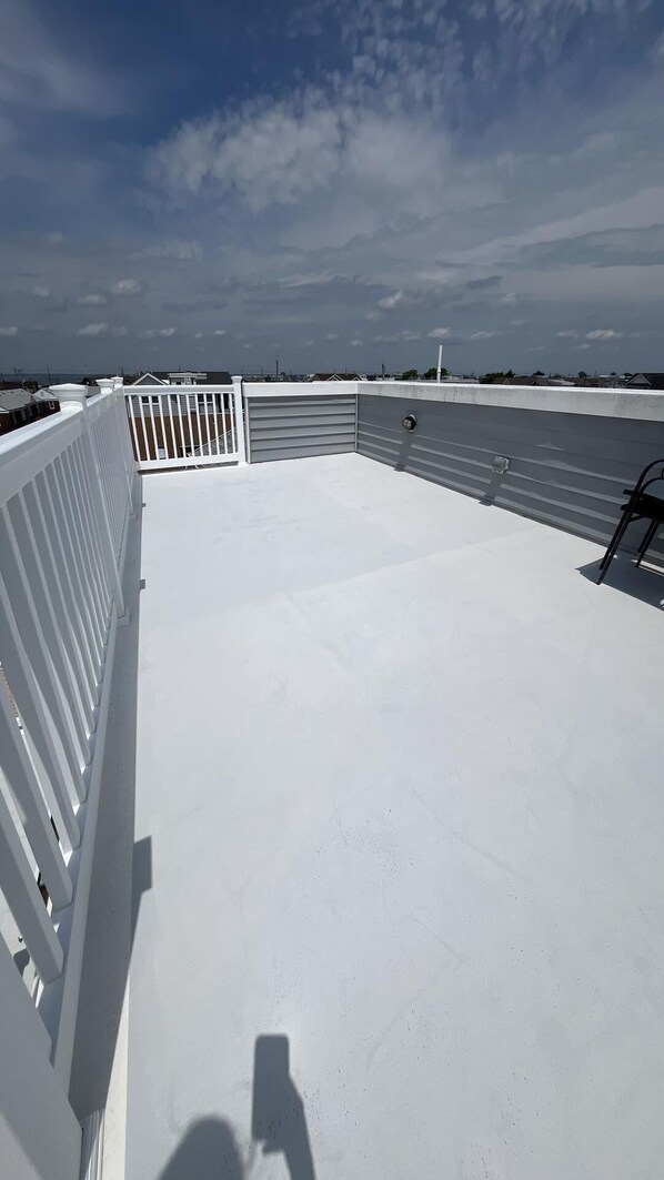 Une terrasse sur le toit avec une balustrade blanche, une porte de garage fermée et un ciel dégagé.