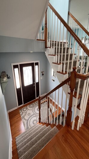 Un intérieur de maison à plusieurs niveaux, avec un escalier, des planchers en bois et un tapis à motifs.