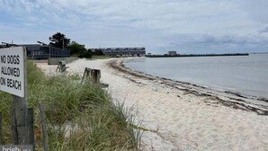 A beach with a sign prohibiting dogs, a wooden fence, and buildings in the background. - LBI vacation rental property (Holgate)