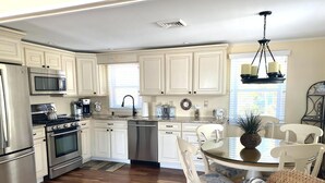 A modern kitchen with white cabinets, stainless steel appliances, a dining area with a glass table, and wicker furniture. - LBI vacation rental property (Holgate)