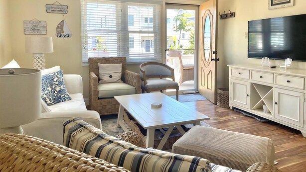 A living room with a sofa, armchairs, a coffee table, a TV, and a door leading outside. - LBI vacation rental property (Holgate)