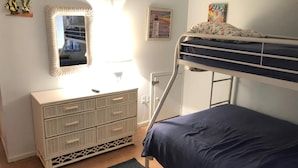 Ein Etagenbett mit blauer Matratze, eine Kommode mit Schubladen, ein Spiegel und ein gerahmtes Bild an der Wand.