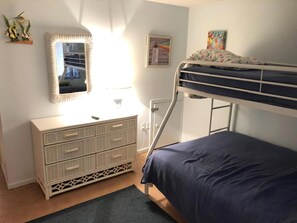 A bunk bed with a blue mattress, a dresser with drawers, a mirror, and a framed picture on the wall.