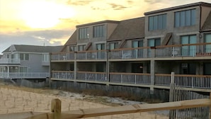 Ein mehrstöckiges Wohngebäude mit Balkonen, einer Holzterrasse und einem Sandstrand im Vordergrund.