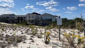 A beachfront property with multiple houses, sandy dunes, and a clear sky.