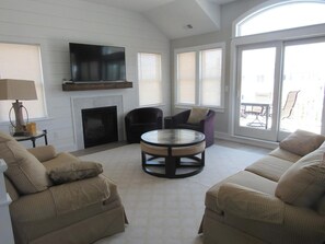 Una sala de estar con chimenea, una mesa redonda de vidrio, dos sofás y un televisor sobre la chimenea.